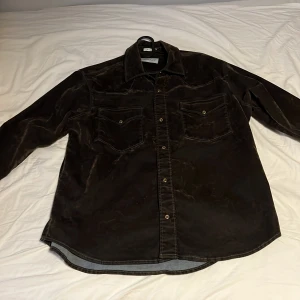 Mörkbrun overshirt från GANT - Säljer en brun overshirt från GANT i oversized fit. Skjortan har långa ärmar, två bröstfickor med lock och knappar framtill. Perfekt att slänga över en t-shirt för en avslappnad look. Jag köpte den för 2500 kr.