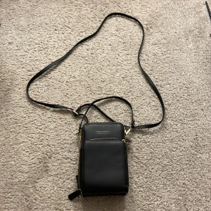 Svart axelväska från Forever MiyiN - Denna touch screen på den plastiga sidan så du lägger i mobilen så kan du chatta eller ringa så du kan sätta på mobilen när du har den i väskan Snygg svart axelväska från Forever MiyiN med flera dragkedjor och en transparent ficka på baksidan. Perfekt för att hålla ordning på dina saker. Väskan har en justerbar axelrem för bekväm användning.