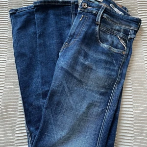 Blå slim fit jeans från Replay Anbass - Säljer ett par snygga blå jeans från Replay, modell Anbass. Jeansen har slim fit passform, klassiska fem fickor och snygga slitningar framtill. Märkesdetaljer på fickan och bak med Replay-läderpatch. Perfekta för dig som gillar stilrena jeans med lite edge. Storlek 29/30, ny skick!