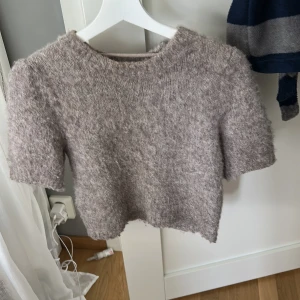 Beige stickad croppad tröja från Vero Moda - Supermjuk och fluffig beige stickad tröja från Vero Moda. Modellen är croppad med korta puffärmar och rund halsringning. Perfekt för att ge en mysig men trendig look till din outfit. Storlek xs.