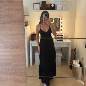 Svart långklänning - Elegant svart långklänning med smala axelband och v-ringning. Den är i storlek S och köpt från Gina. 