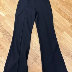 Svarta vida byxor från Vila - Snygga svarta byxor från Vila med utsvängda ben och hög midja. Perfekta för dig som gillar en stilren look med lite extra attityd. Byxorna har en klassisk passform och är tillverkade i ett mjukt material som sitter skönt hela dagen.