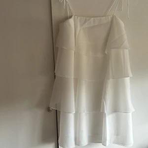 Klänning  - Säljer en söt vit klänning med flera lager av volanger. Klänningen har justerbara band. Aldrig använd.
