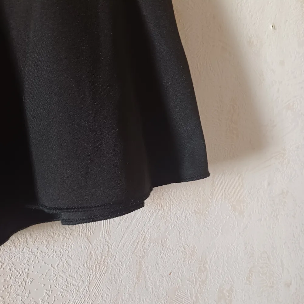 Snygg svart kortkjol med söta rosetter i midjan. Kjolen har en elastisk midja för extra komfort och en lätt utsvängd form som ger en fin siluett. Perfekt för att ge en stilren touch till din outfit.. Hameet.