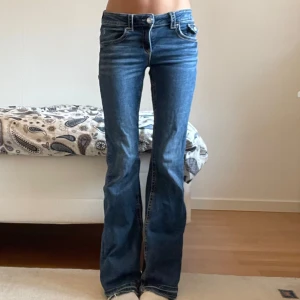 Blå lågmidjade, bootcut jeans från Gina Tricot - Säljer ett par klassiska blå bootcut jeans från Gina Tricot. Jeansen har normal passform, låg midja och utsvängda ben. De är tillverkade i denim med snygga detaljer som kontrastsömmar och fickor bak. Jag har använt de ett par gånger men det finns nästan inga tecken på användning. Jag har även sprättat upp benen längst ner så de passar om man är lite längre. 