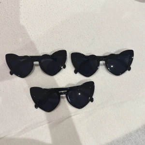 Svarta hjärtformade solglasögon - Säljer coola svarta solglasögon med hjärtformade glas. Perfekta för att ge en lekfull touch till din stil. De har en glansig finish och är lätta att bära.