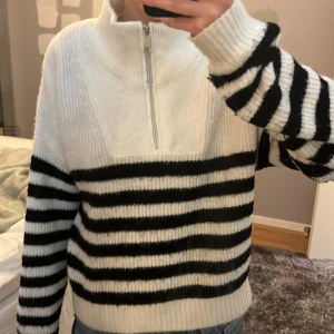 Randig stickad tröja med halv dragkedja  - Säljer en mysig stickad tröja från KappAhl  med svartvita ränder och halv dragkedja framtill. Tröjan har hög krage och långa ärmar. Perfekt för kyliga dagar och enkel att styla med jeans eller kjol. Säljer då den inte kommer till användning längre. ✨