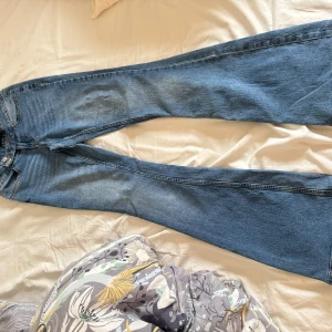 Blå bootcut jeans från Vero Moda - Säljer ett par klassiska blå bootcut jeans från Vero Moda med hög midja och dubbla knappar i midjan. Jeansen har en snygg tvätt och är perfekta för dig som gillar en tidlös stil.