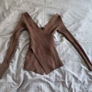 Brun ribbad omlottopp med v-ringning - Säljer en brun ribbad topp med lång ärm och snygg v-ringning. Toppen har omlottdesign och är figurnära med en lite asymmetrisk nederkant. Det är tajt passform och formar kroppen verkligen (ser mindre ut än själva storleken men stretchig) fast ändå skön och andningsbar. Tröjan tillverkas inte längre och befinner sig i bra skick då den är använd fåtal gånger. Som sagt tröjan ger en hourglass ⏳figur och ser bättre på än på bilderna.