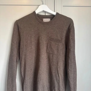Brun tröja från Lexington - Säljer en stilren brun tröja från Lexington med en praktisk bröstficka. Tröjan har långa ärmar och en rund halsringning, perfekt för kyligare dagar. Passar bra till både jeans och chinos. Har ett litet hål i ärmen (se bild).