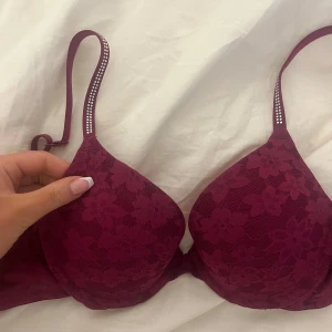 Vinröd push-up bh från Pink  - Säljer en ny vinröd push-up bh från Pink med blommigt spetsmönster och dekorativa stenar på axelbanden. Perfekt för att ge extra lyft och form. Axelbanden är justerbara för bästa passform.
