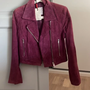 Lila mockajacka från Jofama - Snygg lila bikerjacka i mocka från Jofama. Jackan har en cool asymmetrisk dragkedja och flera dragkedjefickor. Perfekt för att ge din outfit en edgy touch. 💜 säljer då den inte används lappen e kvar också , Ny pris 998 