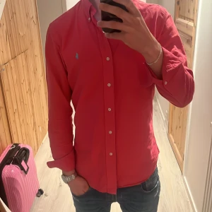 Röd skjorta från Polo Ralph Lauren - Snygg röd skjorta från Polo Ralph Lauren i slim fit. Skjortan har långa ärmar och knappar framtill. Perfekt för en stilren look.