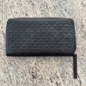 Svart plånbok från By Malene Birger - Snygg svart plånbok från By Malene Birger med präglat mönster och guldfärgad dragkedja. Plånboken har flera kortfack och ett innerfack med dragkedja. Perfekt för att hålla ordning på kort och kontanter.