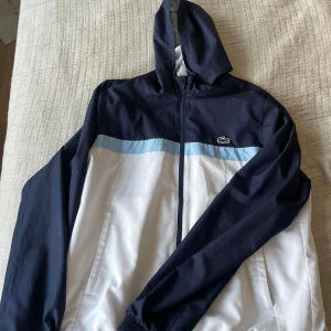 Blå och vit vindjacka från Lacoste - Vindjacka från Lacoste, har ej någon användning av den och den tar bara plats, tveka ej på att höra av er vid frågor!