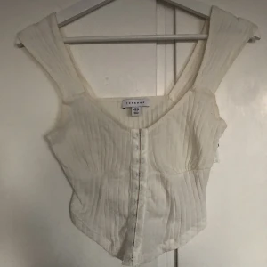 Korsett topp - Korsettliknande topp i ribbat bomullstyg, stretchig. Naturvit färg och knäpps med hakar framtill. Passar stl 36/38, spårbar frakt tillkommer