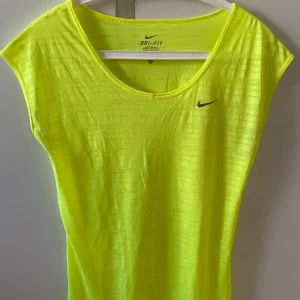 Nike Träningstopp stl XS Neongul - Träningstopp från Nike i neongul färg. Endast använd ett fåtal gånger. Storlek XS men upplevs som S. Lätt genomskinlig med tunt och luftigt material :)