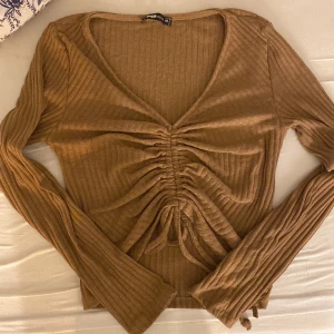 Topp - En brun super fin ribbad topp som man kan anpassa och då dra åt på magen. Storlek M 