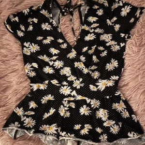 Tröja - En svart sommar topp med blommor på. Den har en liten öppning i ryggen och är från H&M. Storleken är XS men jag tycker nästan att den passar som en S då den är väldigt stretchig. Skriv privat för bild på passform samt måtten! 