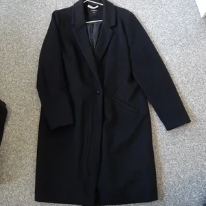 Ullkappa med enkel knäppning - Rak, svart ullkappa med enkel knäppning. Extraknapp finns, både ytterknapp och innerknapp. Jag har gjort en förstärkning av hängaren i skinn 