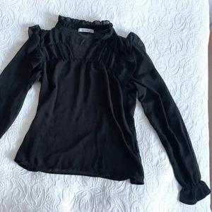 Svart genomskinlig blus - En svart blus som är genomskinlig i tyget från NA-KD i storlek 38. Den har en liten högre krage upptill som är öppen. Den har volangdetaljer och är passande till festligare sammanhang! Den är i jättebra skick och använd en gång! 