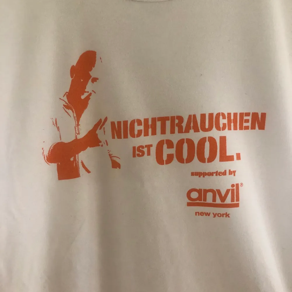 En vit t shirt med orange tryck med texten ”rauchen ist nicht cool”. Texten är på tyska och betyder ”röka är inte coolt. Tshirten är lite vintage och har ingen märkbar skada. Passformen är normal med lite mer äldre passform. . T-shirts.