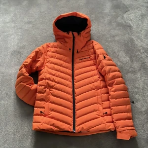 PeakPerformance dunjacka/skidjacka - PeakPerformance mest populära skidjacka det senaste decenniet. Orange i storlek S. Använd ett fåtal gånger då den är lite för liten till min man.. så i nyskick kan man säga! Ficka till liftkort på ärmen. Två sidofickor fram, en innerficka. Snölås i midjan
