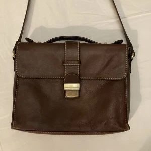 Brun läder axelremsväska - Säljer denna bruna axelremsväska med gulddetaljer från Sellpy. Finns flera fack innuti, det är bara att fråga om fler bilder🥰