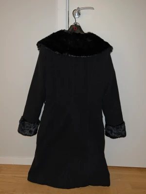 Svart kappa - Fin svart kappa med fusk päls.  Den är upp till knäna, i Storlek XL men passar även L.   Priset kan sänkas vid snabb och smidig affär.✨
