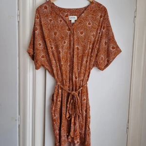 Mönstrad klänning Monki  - Tjusig klänning som passar både till vardags och fest.  Knappt använd. Rostorange grund med ljusare solrosor på.  Stl M men passar även L.  Generös vid midjan och i ärmarna. Regleras med knytband i midjan.  V-ringad. Fickor. Känns luftig, men inte tunn. 