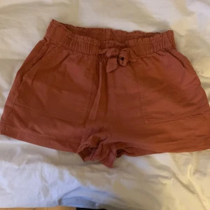 Tygshorts från hm - Säljer ett par jättefina tegelröda tygshorts från hm som är jättesköna på sommaren! Shortsen är streshiga i midjan💞 De är strl 158-164, men passar nog de som har xs och kanske t.o.m. s🫶🏻 Har inte använts särskilt mycket pga att de inte riktigt är min stil☺️
