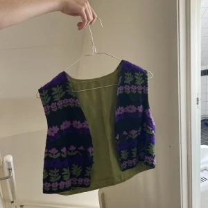 Lila väst - Svart kort väst med lila broderade blommor och löv. Säljer pga ingen användning 