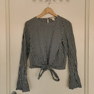 Randig blus - Randig blus från H&M i tyg med lite struktur likt bäckebölja. Fin detalj med knyte framtill  Storlek 36.