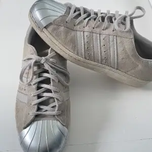 Säljer ett par adidas skor i grå färg. Väldigt fint skick och har en metall bit längst fram på skorn! 