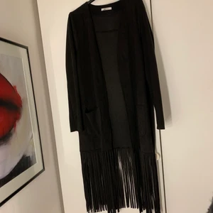 Kofta i mockaimitation och fransar - Lång kofta i mockaimitation med fransar nedtill och två fickor på varsin framsida. Går nedanför knänen på mig som är 1,75 lång. Köpt från Gina tricot. Använd flera gånger men hållit sig som i nyskick ändå. Jättefin och skön dessutom