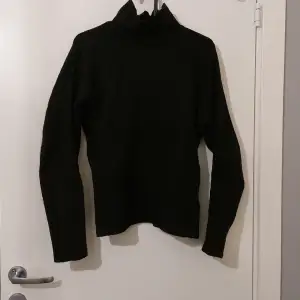 En vanlig svart tröja med hög nacke och slit på armarna