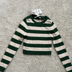 Randig långärmad tröja - En randig tröja i mörkgrön och naturvit (se andra bilden). Den är croppad och går till strax över navlen. Aningen mindre i storlek så jag som brukar ha S kan ha denna. Aldrig använd och säljer pga att det är inte min stil och kunde inte lämna tillbaka. Köparen står för valfri frakt, pris kan diskuteras. Skriv för mer info eller bilder. 