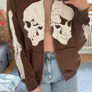 Brun zipper hoodie med skelett tryck! - säljer den här för att jag sällan använder den! men skit cool:) Hoodien är ganska så tun, går ungefär till skrevet & har luva. (Baksidan har inget tryck) Den är i storlek M men skulle mer säga att den sitter som en S.