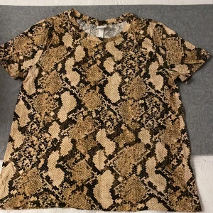 Ormmönstrad t-shirt - En t-shirt med kort ärm, klassiskt rund halsringning, rak passform, 100% mjuk bomull Längd ca. 55 cm i stl EU small. Ormmönstrad . Finskick. 