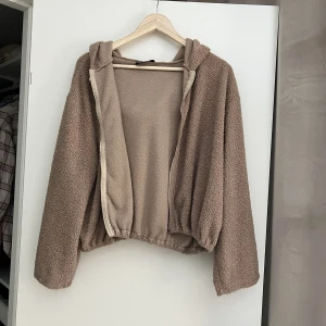 Beige/brun teddy  - Beige/brun teddy med luva och dragkedja. Utvsvängda armar. I gott skick! Samfraktar gärna! Kolla in mina andra annonser om det finns något av intresse!