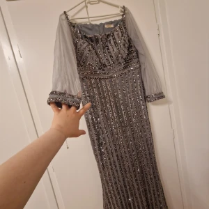 Fest klänning - Fest lång klänning, meramid shape använd bara en gång för 4 timmar ,nästan ny,passar så bra med storlek från 38 /46 ..det finns möjlighet att för långa klänningen också stora det runt om axlarna fargen är glliterd grå  köppt för 4500kr ska säljas för 2000