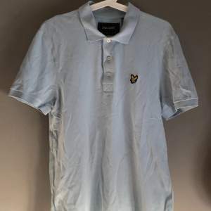 En ljusblå pikétröja/kortärmad skjorta i storlek medium. Märke: lyle & scott