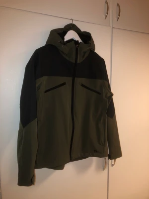 Skaljacka grön/svart - Grön och svart outdoor/skaljacka oanvänd och helt i nyskick. Softshell material. Dragkedja i fickor och innerficka. Bra skydd mot vind och regn.