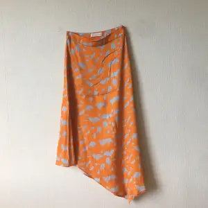 En underbar kjol från Mykke Hoffman i assymetrisk midi-modell. Materialet är lätt och mjukt, så skönt att bära på sommaren. Färgställningen är orange och ljust silverblå. Knappt använd, mycket bra skick!