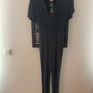 NLYONE lång glittrig byxdress - En lång och glittrig byxdress från NLYONE. Djup skärning både fram och bak. Köparen betalar frakt. Aldrig använd. 