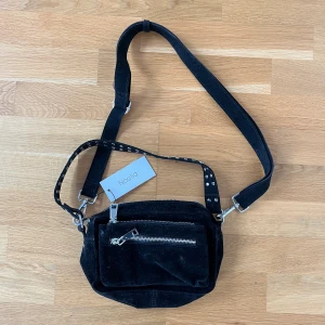 Noela crossbody bag - En svart crossbody väska från Noella. Svart med knappar och har 2 mindre fack och ett stort. Banden går att justera och den är helt oanvänd! Köparen står för frakten💖