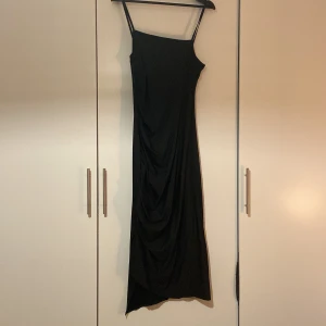 Klänning  - Svart tunn lång klänning med liten slits och lite sne sydd figur, även veckad framsida. Aldrig använd, endast testad. Storlek 38/40. Ganska mycket resor i den. 
