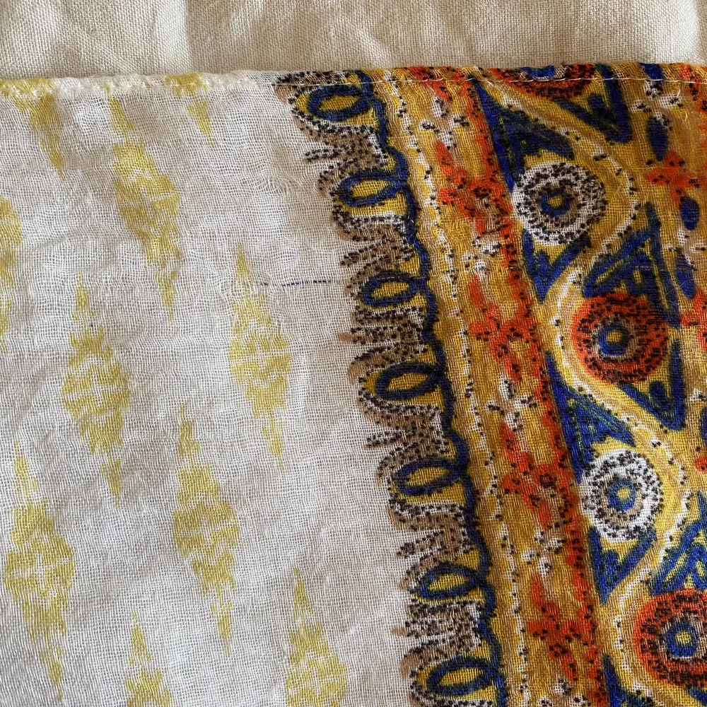 En tunn sjal med mönster i gult, blått och oranget. Köpt på marknad i Thailand så jag vet inte vad det är för slags material. Men det är ett väldigt mjukt och skönt tyg. Tunt men värmande.   Finns en del små revor.   Mått:  - B: 90 cm - L: 170 cm . Övrigt.