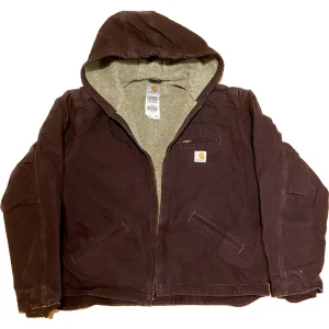 Carharrt hooded jacket - En unik lila, åt det bruna hållet, carharttjacka som är fodrad och har luva. Fickor finns även på insidan av jackan. Gjord i USA. Väldigt bra skick.  Mått; Bredd (61), Längd (58), armar(55).