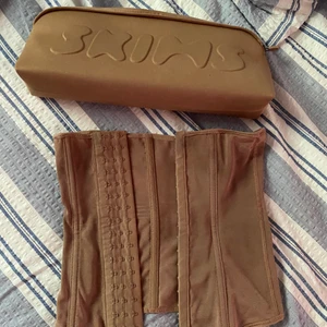 SKIMS korsett/waist trainer - En beige korsett/waist trainer från Kim Kardashians märke SKIMS. Köpt förra året, i använt skick. Går att tvätta i maskin. Inte stel eller jobbig att ha på sig, säljs endast då den inte längre används